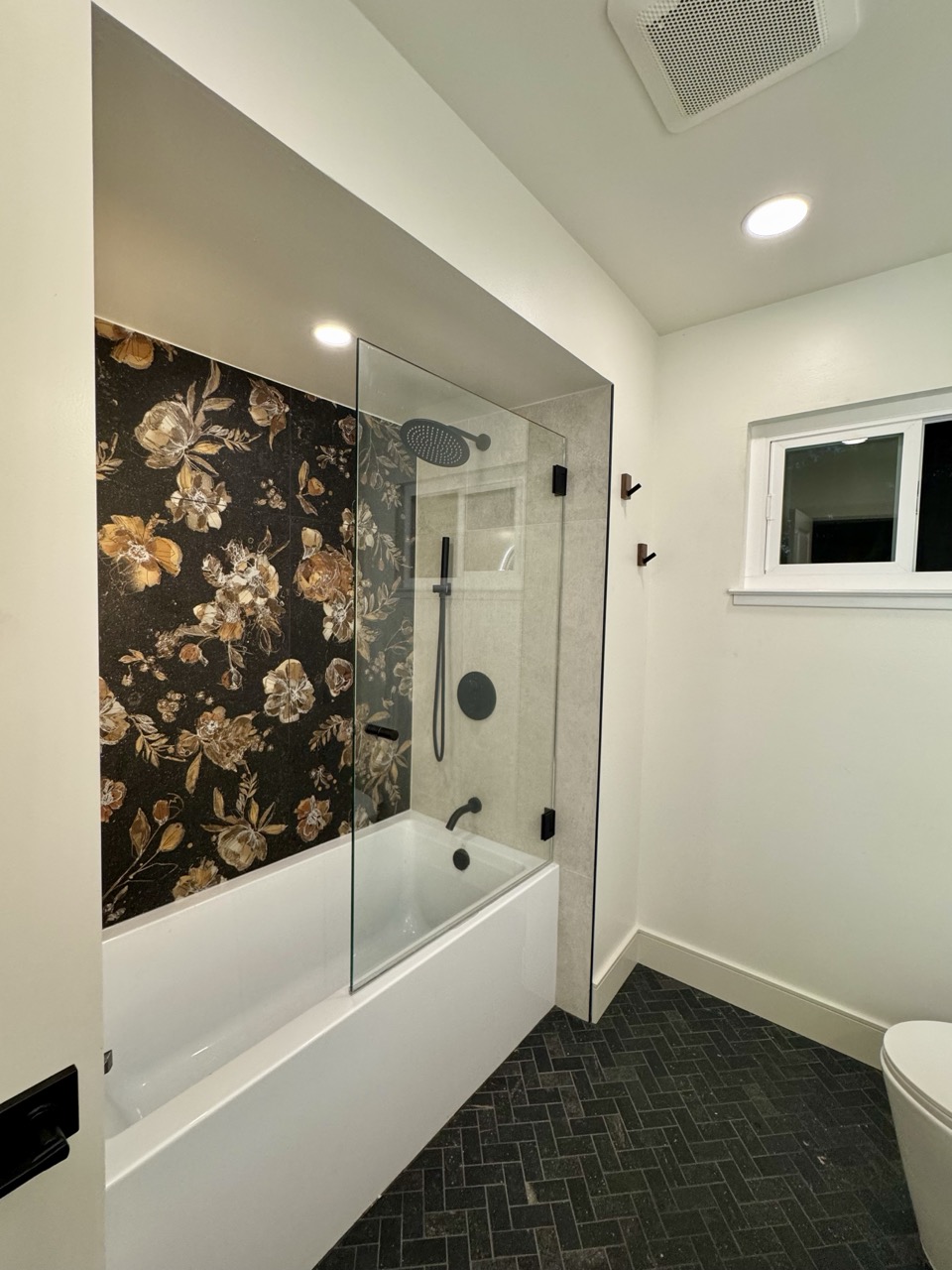 Guest bath after — glass shower panel and dark floral tub surround